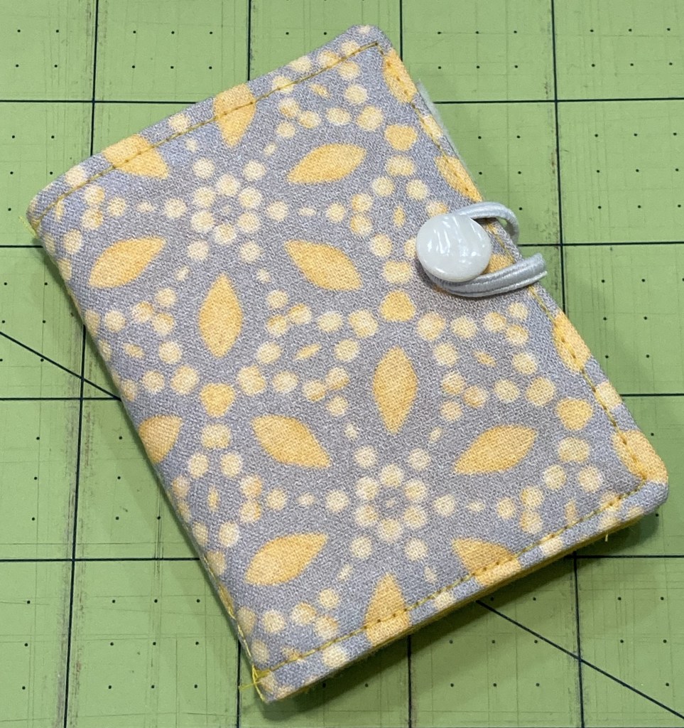 A handmade sewing needle book made with yellow and gray printed fabric.